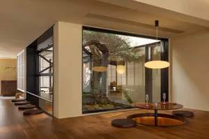 A modern minimalist lounge featuring a glass-enclosed atrium with a tree, wooden floor, and metal furniture.