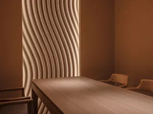 A minimalist interior design featuring wooden furniture and a wave-patterned wood panel wall.