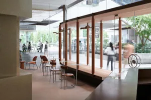 A modern cafe interior featuring glass walls, wooden tables, and chairs.
