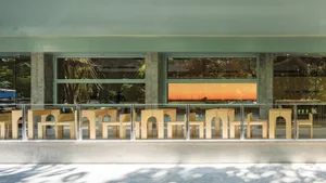 A modern restaurant exterior featuring wooden furniture and large glass windows.