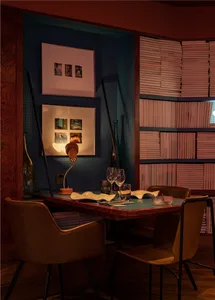 Modern restaurant interior with wood furniture, leather chairs, glass bottles, and bookshelves filled with books.