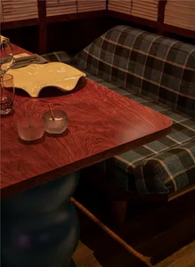 A wooden table with checkered cushions and a glass drink container in a restaurant setting.
