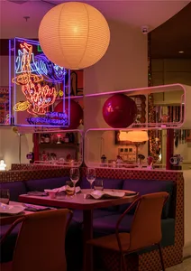 Modern restaurant interior with red and purple lighting, fabric seating, and wood accents