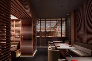 A modern restaurant interior with wooden paneled walls, white upholstered seating, and red plates on the tables.