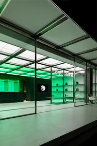 An exterior view of a modern retail storefront with a green illuminated interior featuring minimalist glass walls