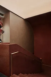 A modern staircase with red-painted concrete walls and stairs, featuring a curved design and a glass railing.