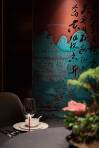A table setting in a restaurant with a paper screen displaying Chinese calligraphy and a plant.
