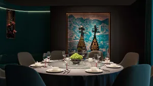 A round dining table set for six in a restaurant dining room, featuring a textured wall covering, glass tabletop, and upholst