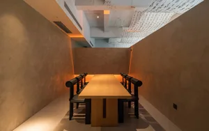 A spacious, industrial-style conference room featuring a long wooden table surrounded by black chairs.