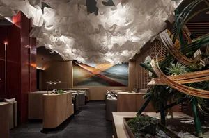 Modern restaurant interior with a white organic cloud ceiling, bamboo structure, and a waterfall fountain centered on a red a