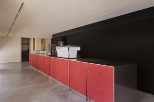 A sleek, modern coffee shop counter with red metal cabinets and a black surface.