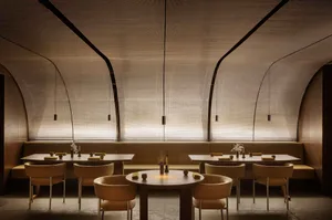 A modern restaurant interior featuring neutral-tones seating and tables adorned with minimalist decor.