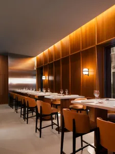 A modern restaurant interior featuring wooden walls and furniture with white countertops and orange stools.