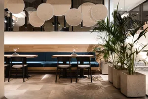 A sleek modern restaurant interior featuring wooden tables, cement planters, and a combination of wood and cement materials.