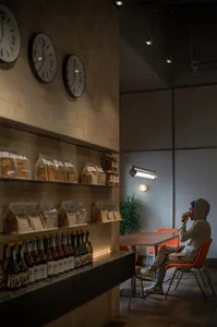 A person sitting at a table in an industrial-style cafe with a concrete wall and shelves displaying packaged products.