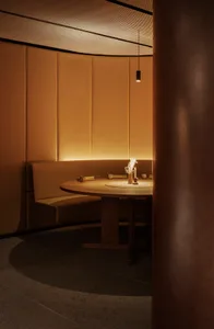 A minimalist restaurant dining room with a round wooden table, leather seating, and warm lighting.