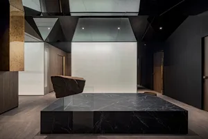 A modern lobby featuring a black marble platform and a black marble rock sculpture.