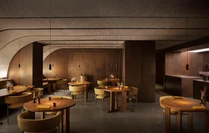 Modern restaurant interior with round wooden tables, yellow cushions, and minimalistic decor.