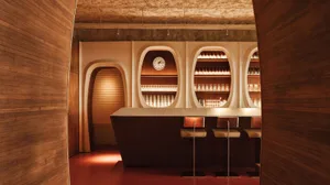 A modern bar interior with a wooden counter, arched walls, and illuminated shelves.