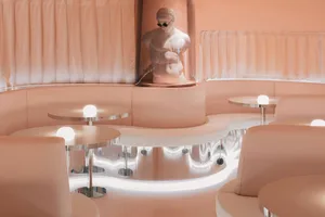 A modern bar interior with pink leather seating and stainless-steel tables.