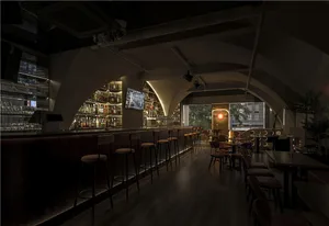 A modern bar interior with wooden and concrete materials and high stools at the bar.