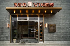Retail storefront with brick exterior, glass doors, and metal accents, illuminated by warm bulbs.