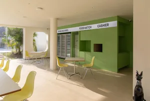A minimalist cafe interior featuring colorful yellow furniture surrounded by green walls and tables.