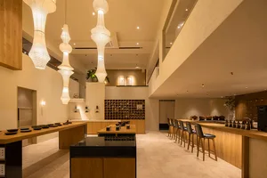 A modern minimalist restaurant interior with wood elements and a high, open ceiling.