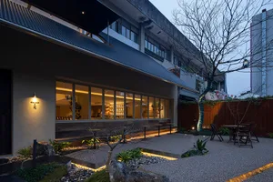 A serene coffee shop courtyard featuring a mix of concrete, glass, and rock materials.