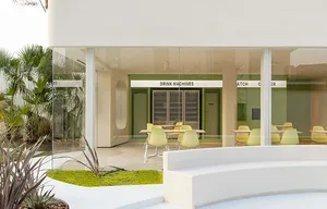 Modern coffee shop patio with glass walls, greenery, and concrete seating.