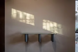 A minimalist glass console table mounted on a wall, casting shadows on the wall.