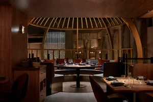 A modern restaurant interior with a combination of concrete and wood materials, featuring round tables and comfortable seatin
