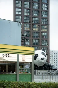 Outdoor view of a modern coffee shop with a large panda sculpture and a high-rise building in the background.