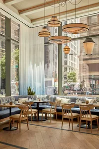 A spacious restaurant interior with industrial and farmhouse design elements, featuring large windows, rustic wooden furnitur