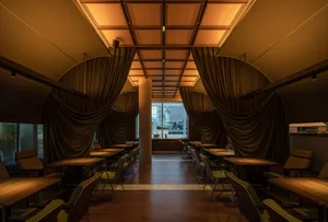 Modern restaurant interior featuring curtains and windows with a wooden floor and sustainable furniture.