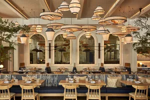 A modern restaurant interior with wooden tables, upholstered benches, and hanging pendant lights.