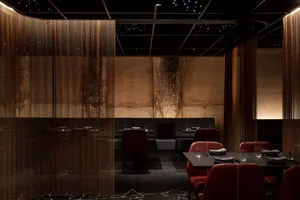 A modern restaurant interior with metal acoustic curtains, dark marble flooring, and dark furniture.