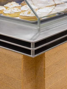 A close-up view of a bakery countertop display featuring a metal case with a glass top, showcasing baked goods with white ici