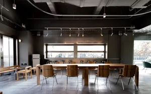 A spacious, minimalist conference room featuring industrial design elements and wood furniture.