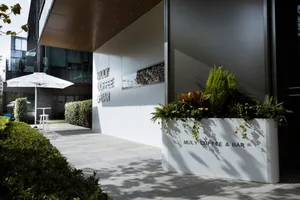 The exterior of a minimalist coffee bar with concrete walls and greenery.