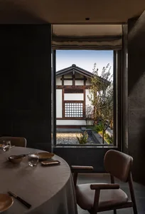 Modern restaurant with concrete floor, minimalist design, and a view of a traditional building through a window.