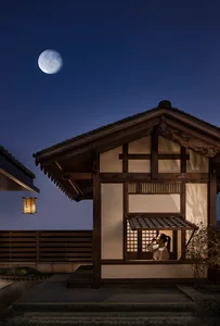 A traditional Japanese wooden structure with a paper lantern hanging outside, under a clear night sky with a full moon.