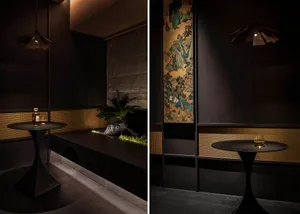 A modern restaurant interior with dark wood, suede, and woven-fiber materials, featuring a dark table with a glass and a smal