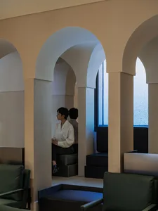 A person in a white shirt sitting in an archway within a concrete interior space.
