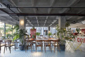 Industrial-style cafe interior with concrete columns, exposed ceiling beams, and plants.