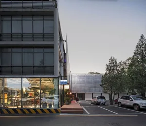 A modern commercial building with a glass facade and a parking lot in front.
