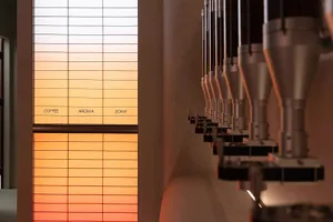 Metalic coffee roasters in a row inside a plant, with a gradient light effect from orange to white.