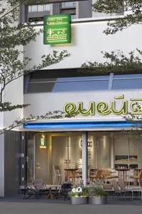 A modern, minimalist café storefront with concrete accents and green signage.