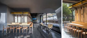An industrial-style restaurant interior featuring wooden tables, metal chairs, and glass panels.