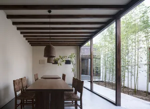 A minimalist dining room with a wooden table and chairs, featuring a wooden ceiling and floor-to-ceiling windows with bamboo 